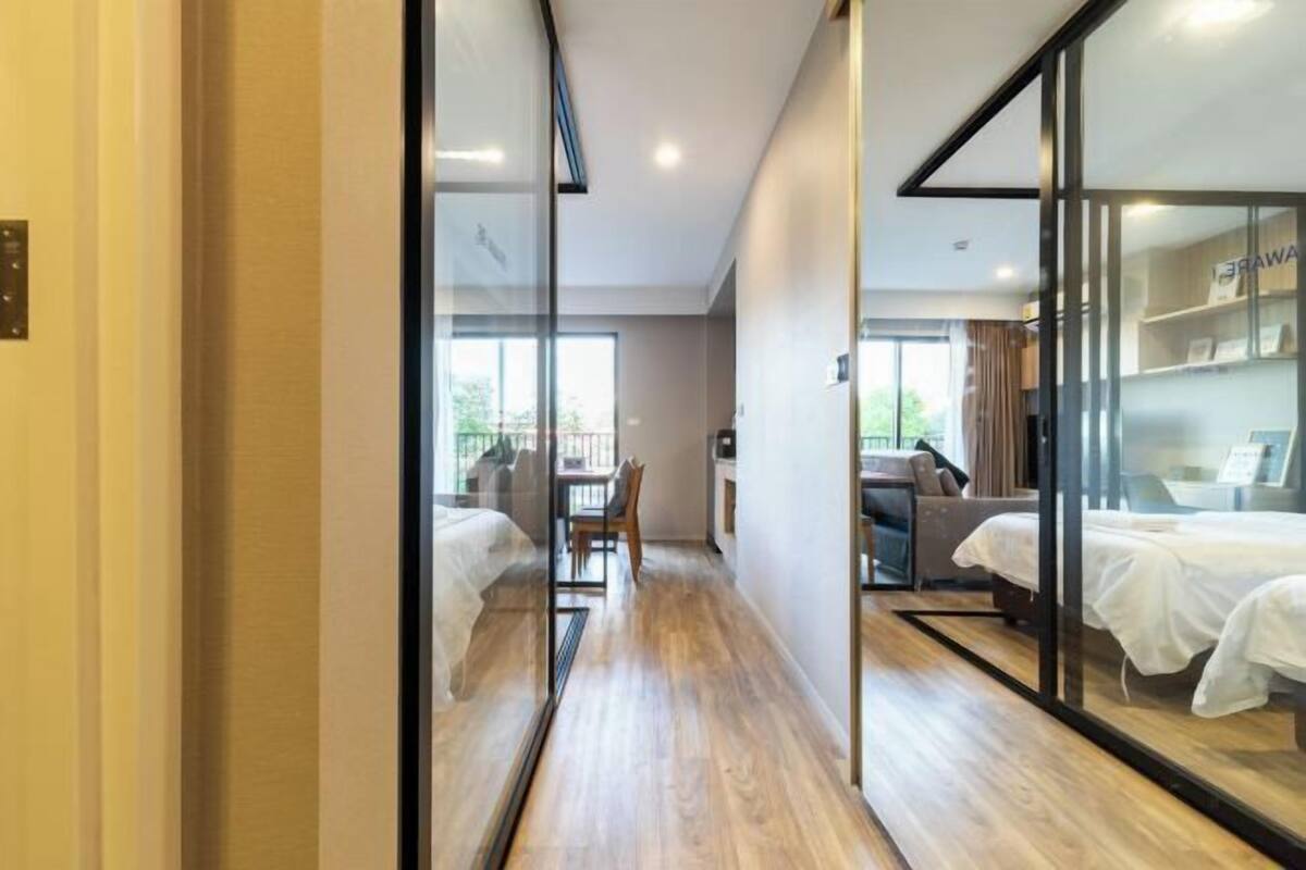 Una habitación de hotel moderna con suelo de madera, separador de vidrio y cama con cubrecama blanco.