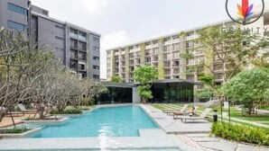 A modern building with a swimming pool surrounded by greenery and lounge chairs.