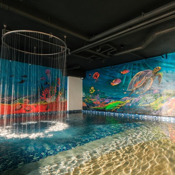 Piscina interior con un mural de vida marina y una fuente de agua.