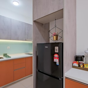 Une cuisine moderne avec un réfrigérateur noir, un luminaire suspendu et un plan de travail sur lequel sont disposés divers objets.