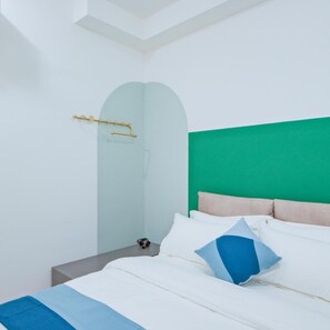 Un dormitorio moderno con cabecera verde, ropa de cama blanca y una mesita de noche con lámpara.