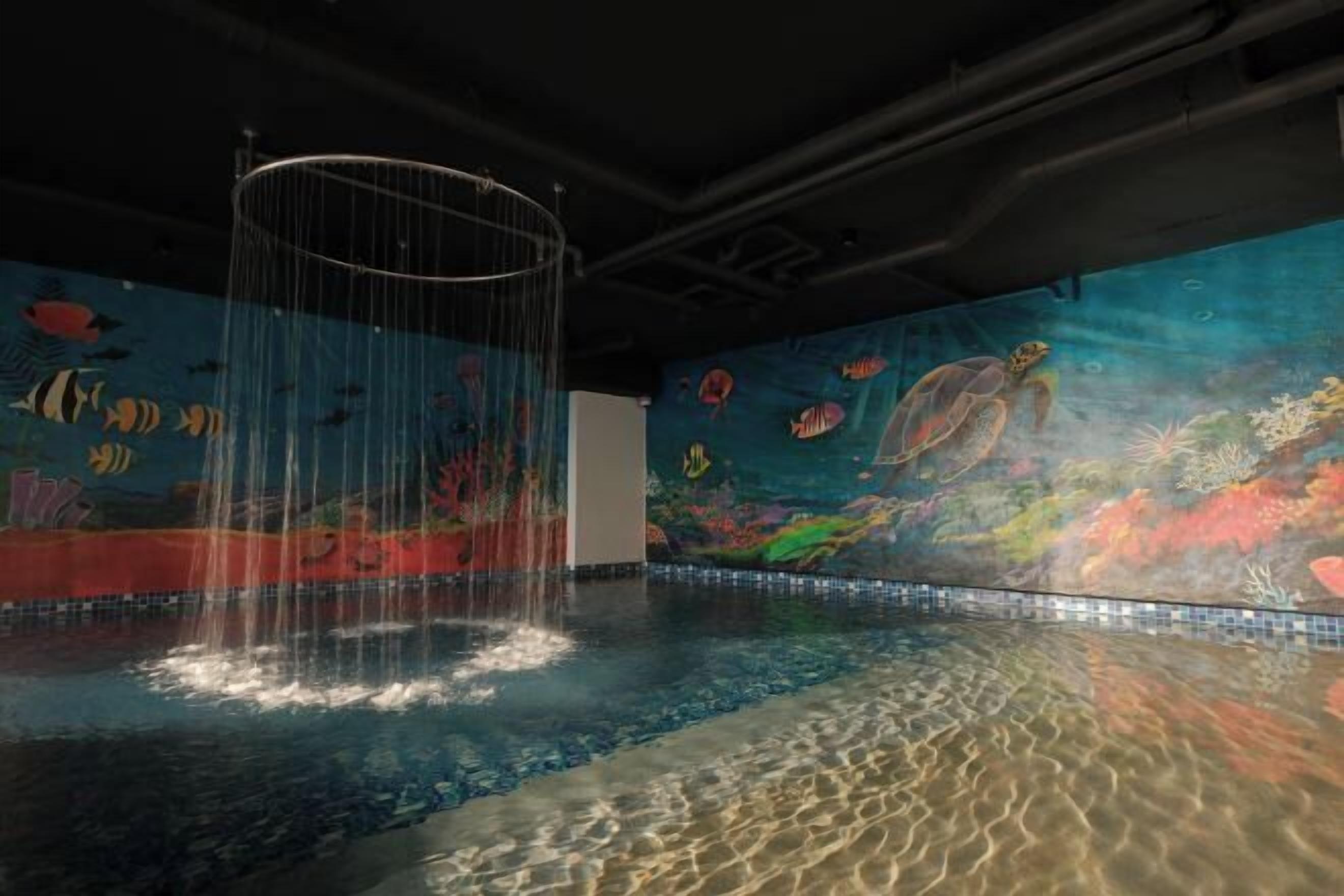 Piscina interior con un mural de una escena submarina, incluyendo peces y una tortuga.