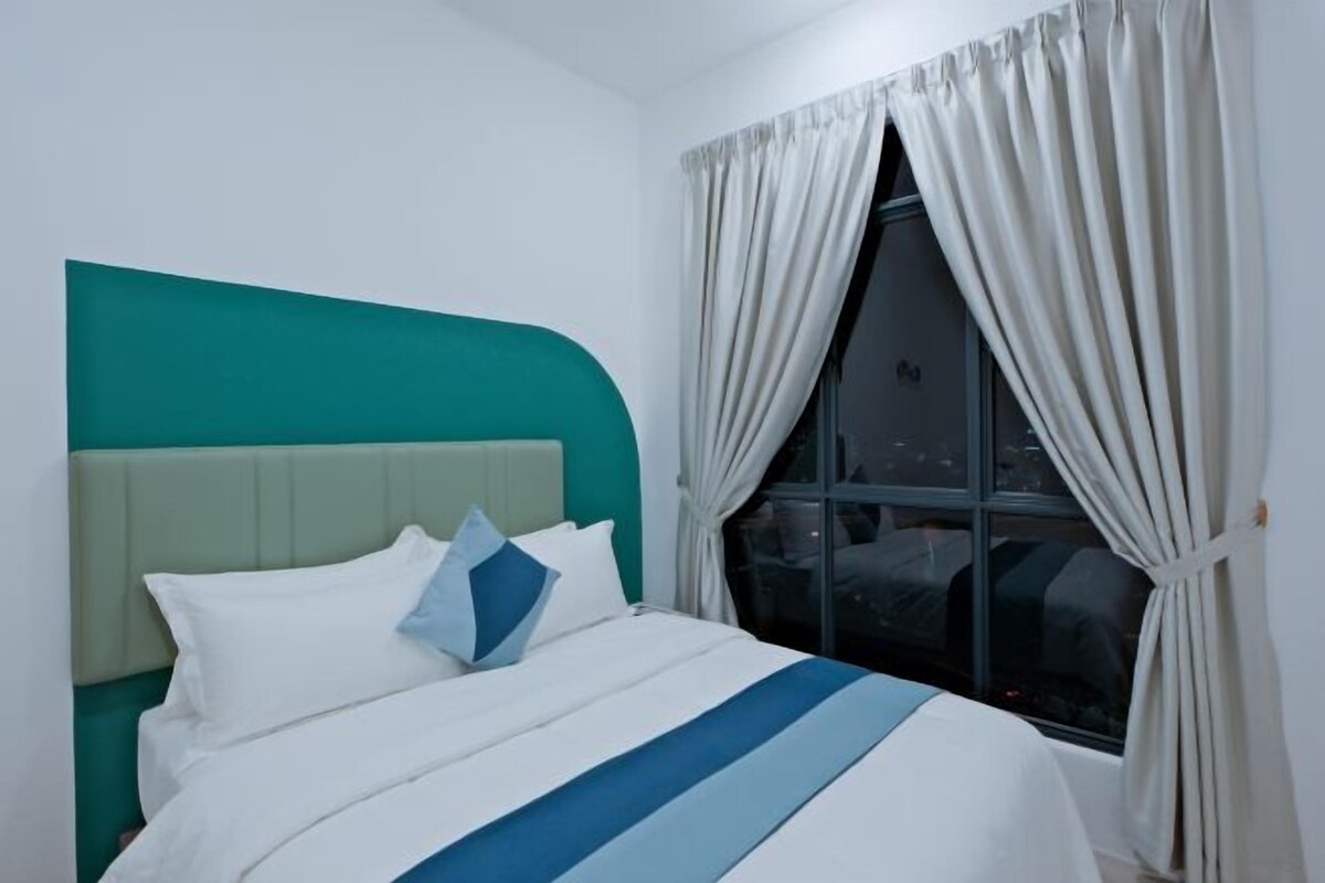 A hotel room with a bed, teal-colored headboard, white and blue striped bedding, and a window with curtains.