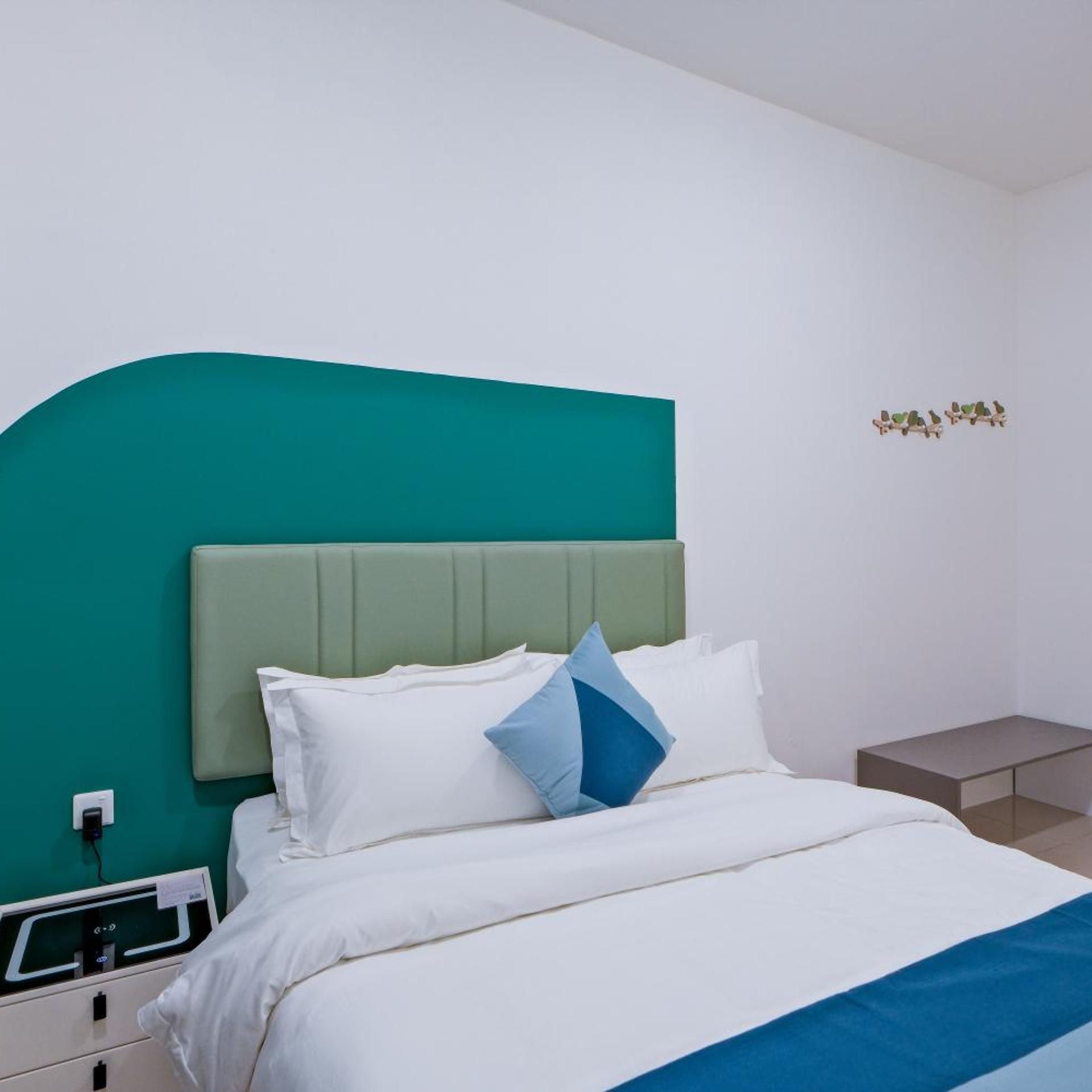 A bed with a teal headboard, white bedding, and a blue accent pillow.
