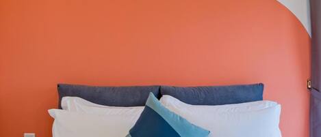 A bed with white bedding and a blue pillow, set against an orange wall.