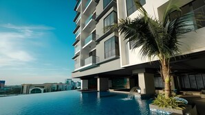 A modern hotel with a swimming pool, a palm tree, and a view of the cityscape. - G Residence Sky Suite (Alor Setar)