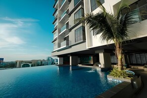 A modern hotel with a swimming pool, a palm tree, and a view of the cityscape. - G Residence Sky Suite (Alor Setar)