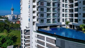 A high-rise building with a rooftop swimming pool and a view of a tower in the background. - G Residence Sky Suite (Alor Setar)