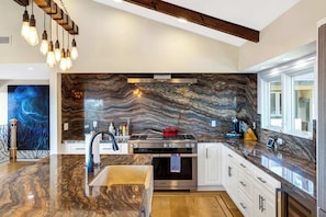 A modern kitchen with a marble backsplash, stainless steel appliances, and a pendant light fixture.