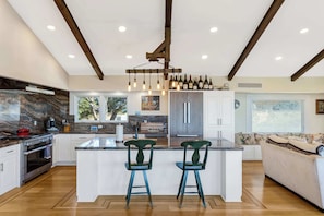 A modern kitchen with a central island, bar stools, and a dining area with a sofa.