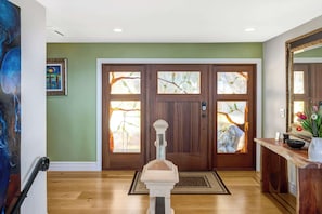 A wooden front door with stained glass panels, a doormat, and a wooden console table with a vase of flowers.