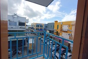 A view from a balcony overlooking a parking lot with several buildings, including a yellow one with signage. - Shoreline Guesthouse (Semporna)