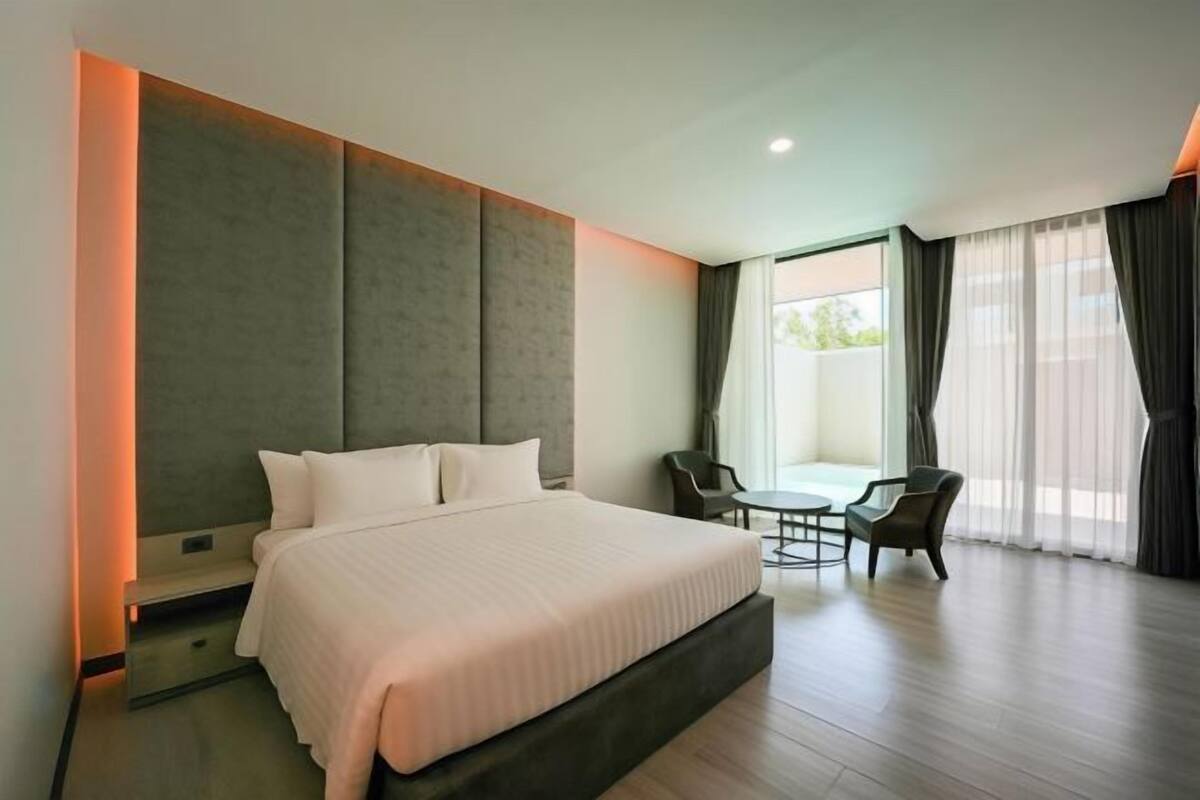 Une chambre d’hôtel moderne, dotée d’un grand lit, d’une petite table, de deux chaises et offrant une vue sur l’extérieur grâce à de grandes fenêtres.