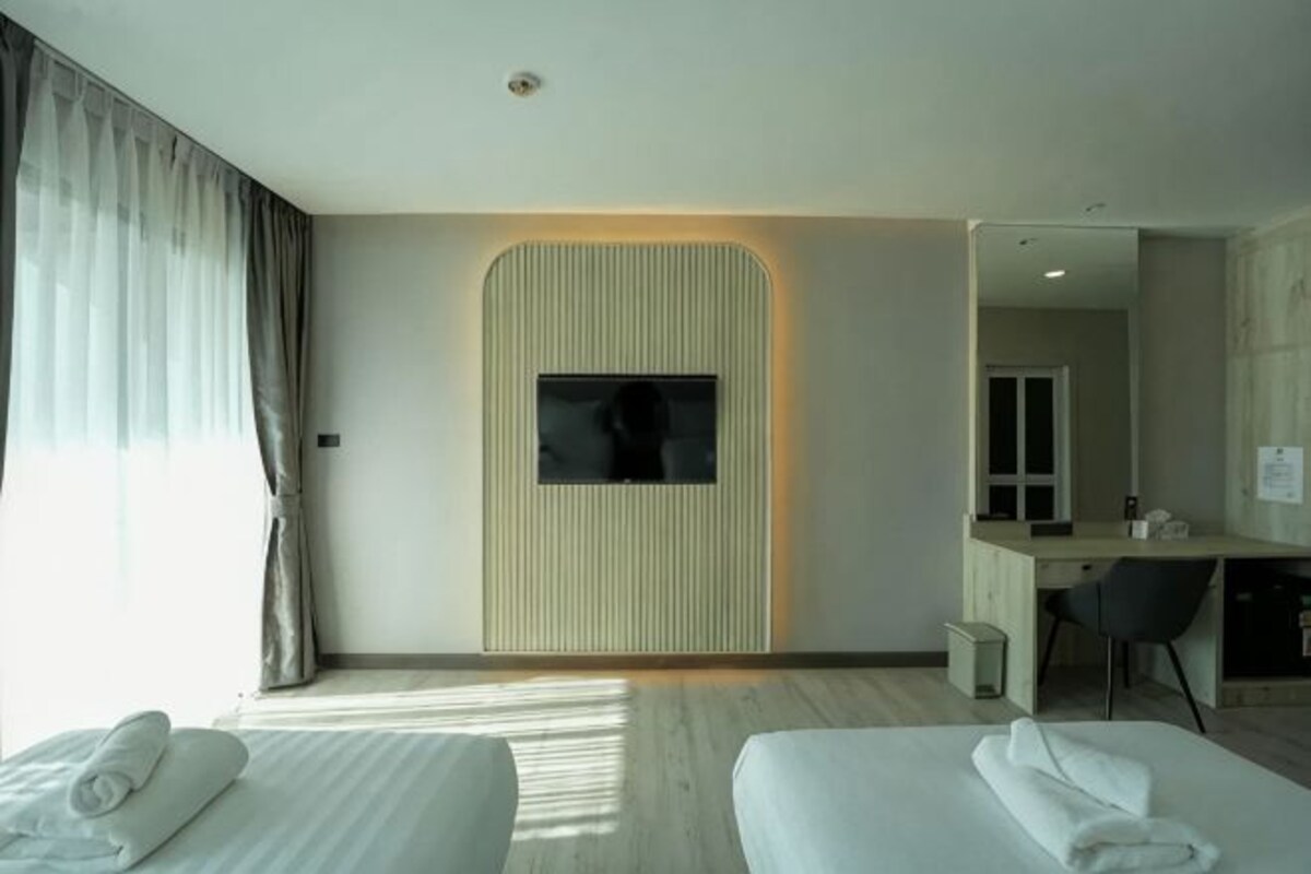 A hotel room with two beds, a desk, a mirror, and a TV mounted on the wall.