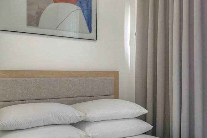 A bed with a headboard and pillows, a framed picture on the wall, and a window with curtains.