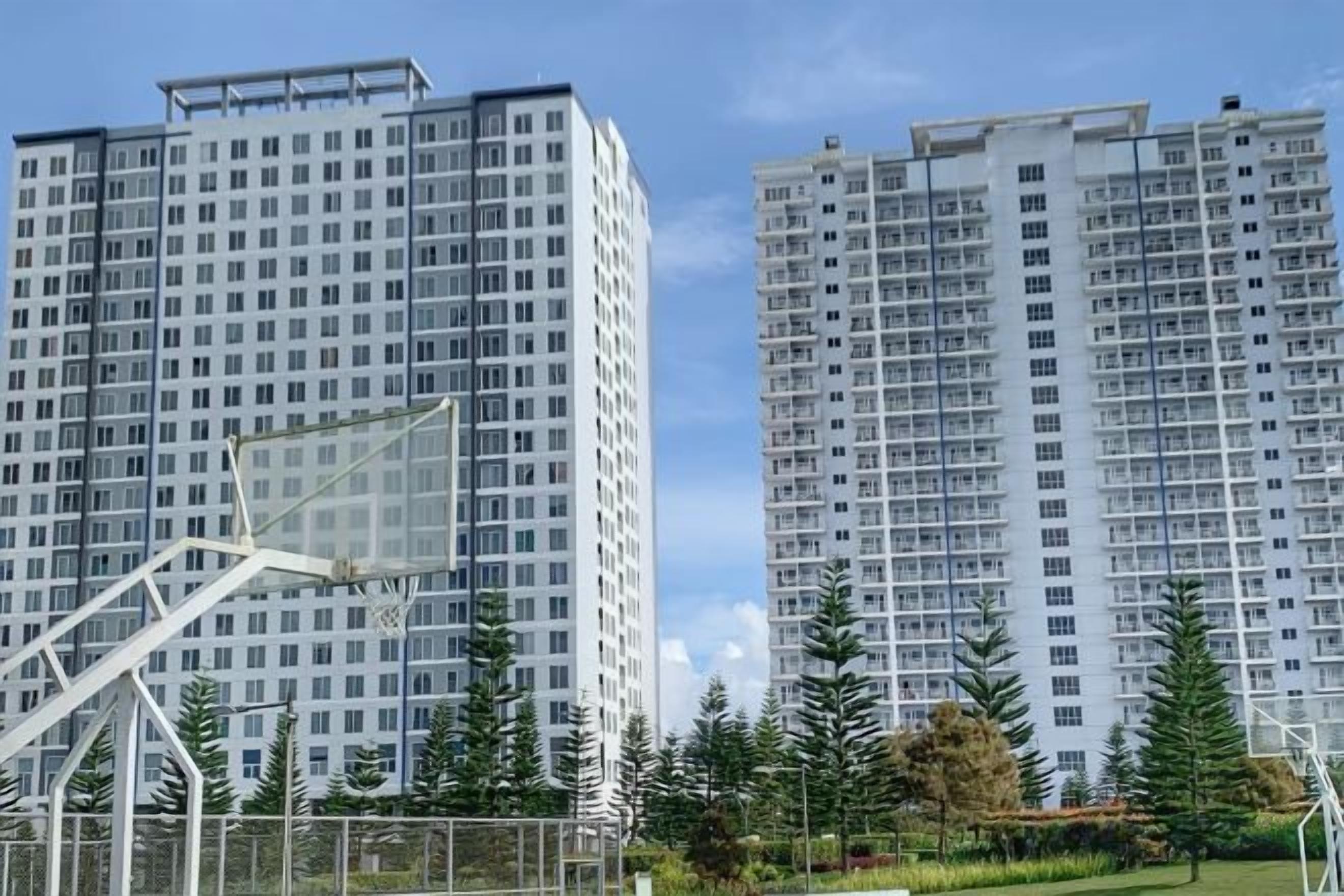 Two high-rise residential buildings with a sports field in the foreground.