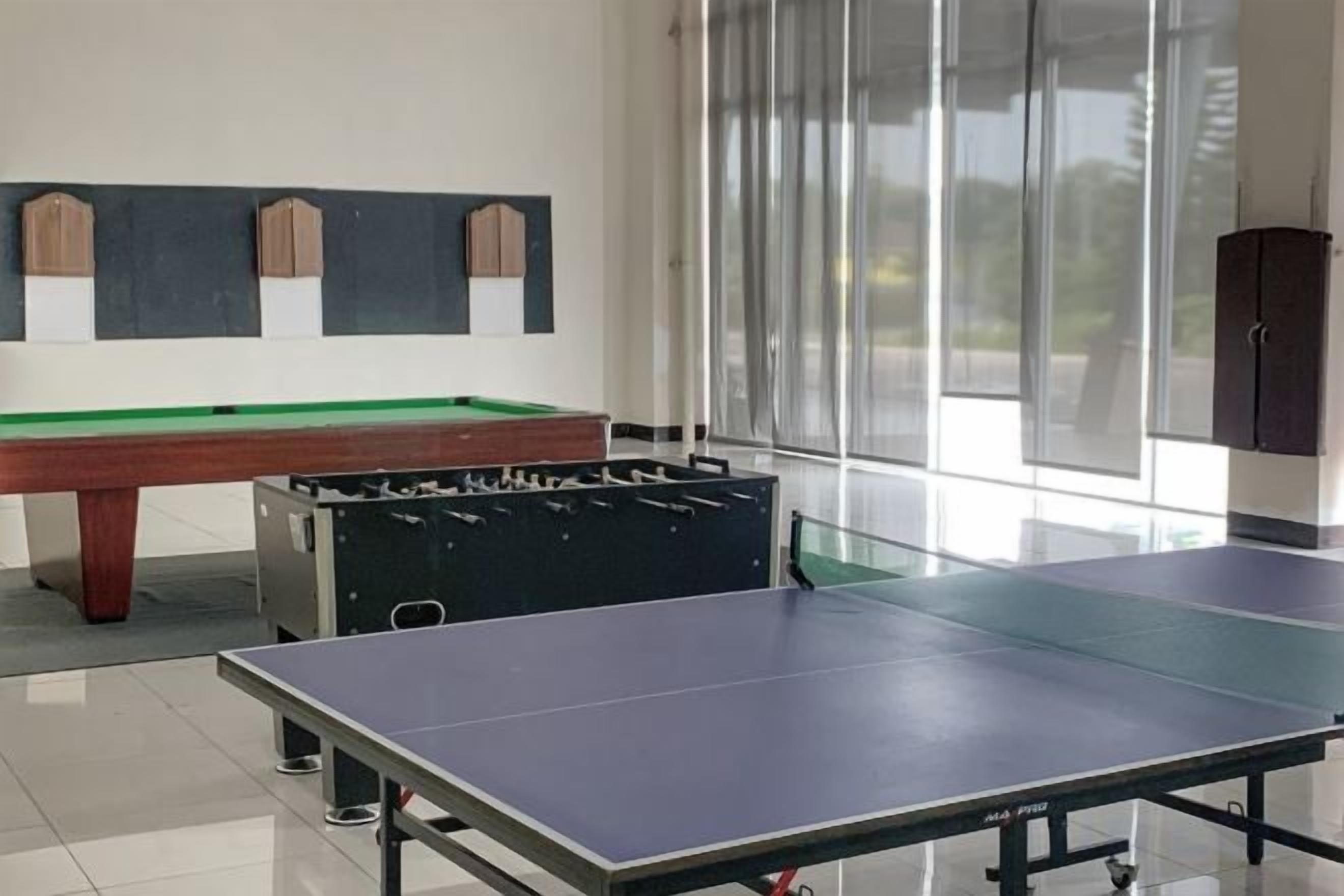 A billiards table, a foosball table, and a ping pong table in a well-lit room with large windows.