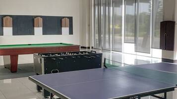 A billiards table, a foosball table, and a ping pong table in a well-lit room with large windows.
