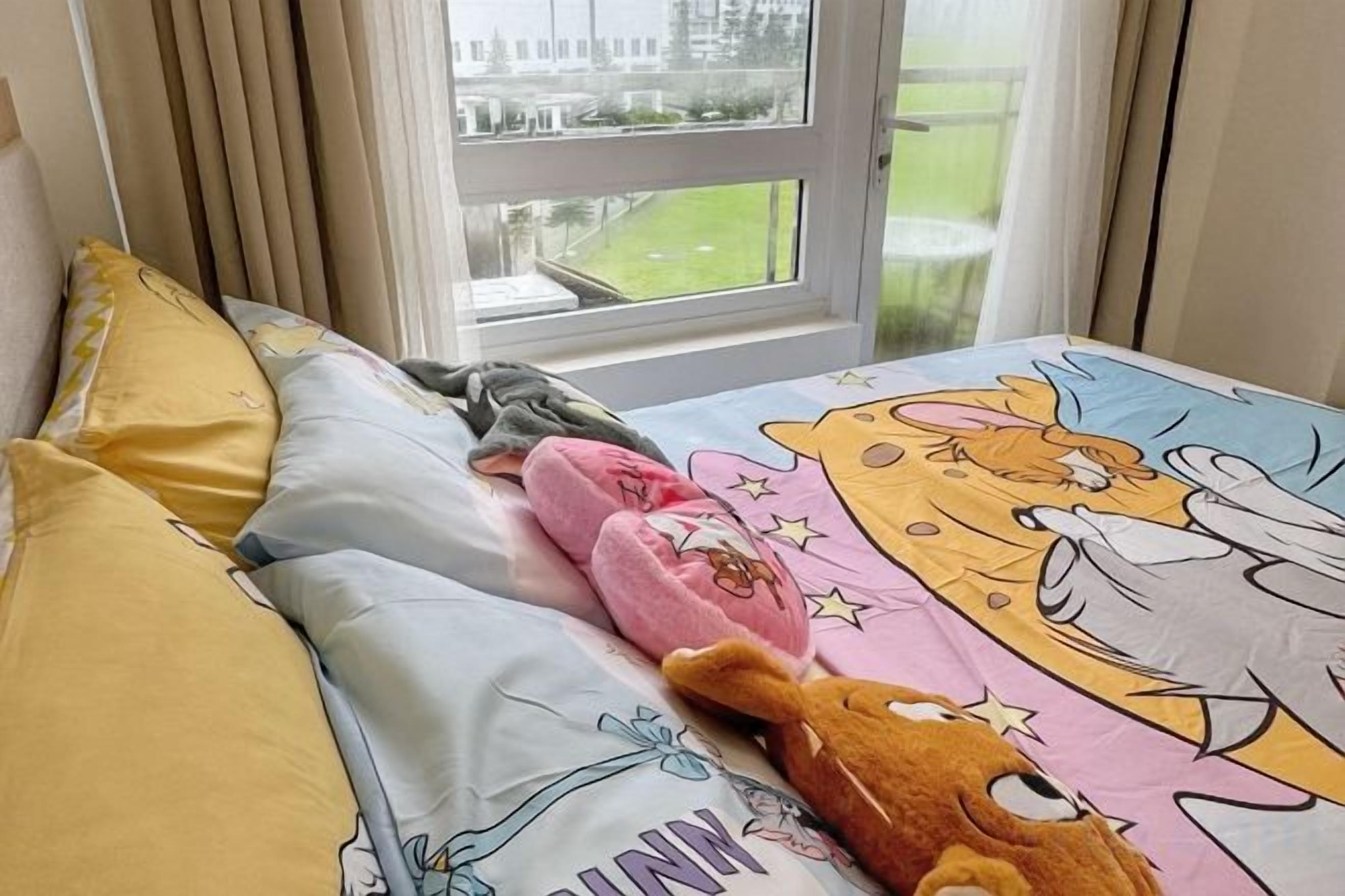 A bed with a colorful cartoon-themed bedspread, pillows, and a stuffed toy.
