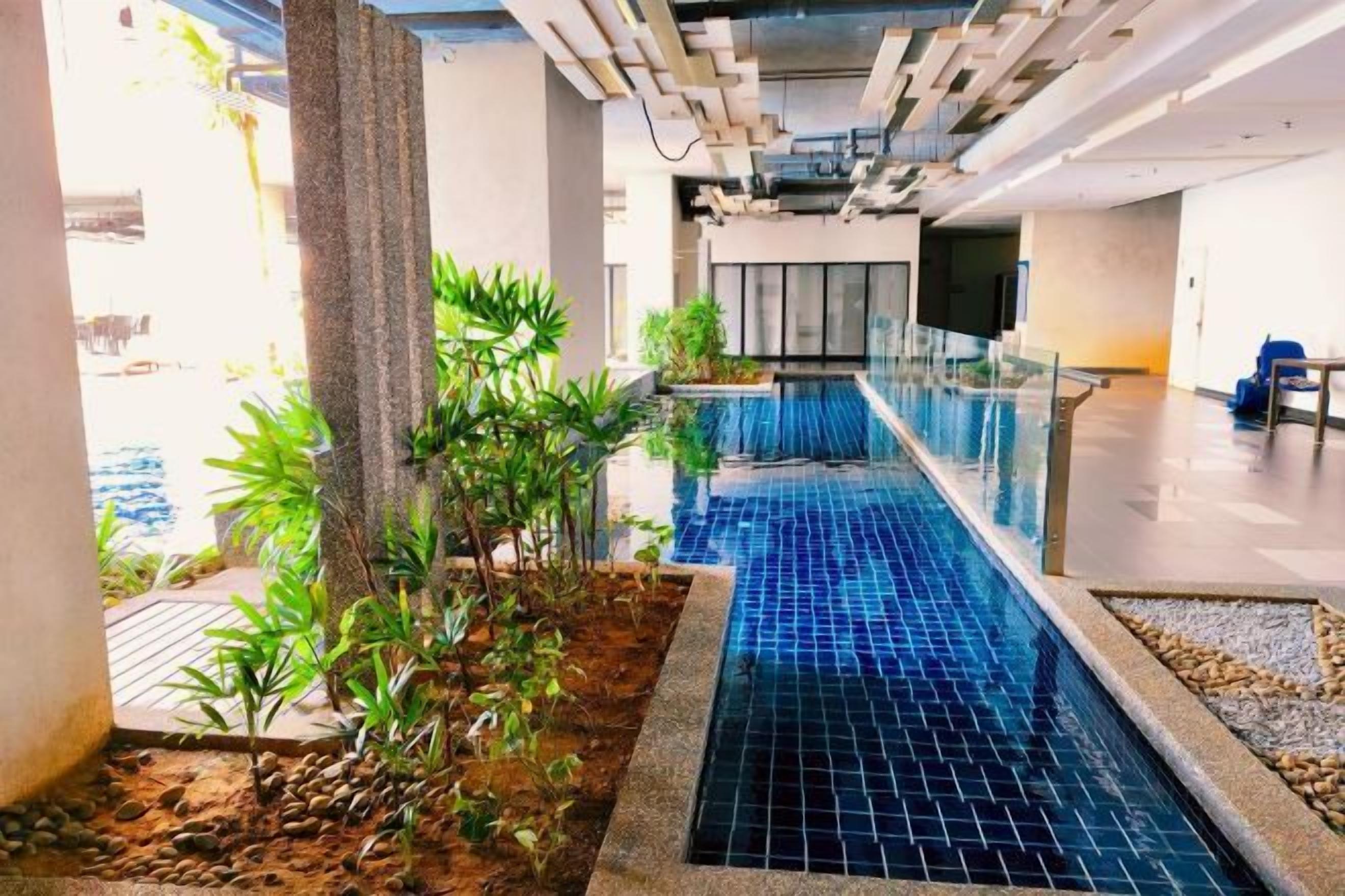 An indoor swimming pool with a tiled floor, surrounded by plants and a modern architectural design.