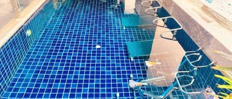 A swimming pool with blue tiles, lounge chairs, and a glass enclosure.