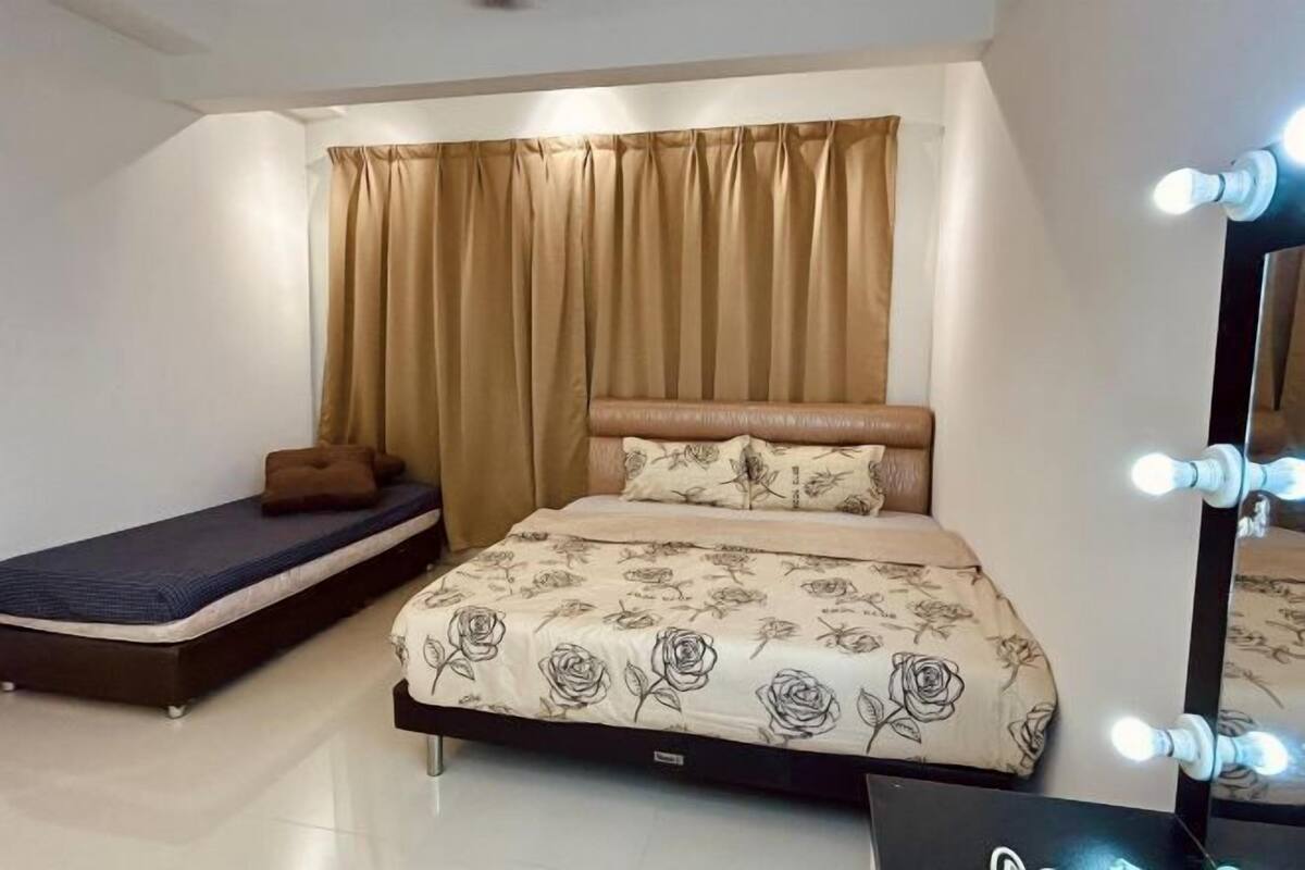 A bedroom with a bed, a smaller bed or sofa, a vanity with lights, and a curtain.