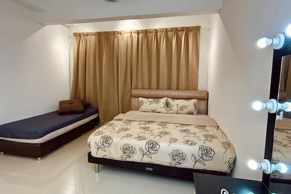 A bedroom with a bed, a smaller bed or sofa, a vanity with lights, and a curtain.