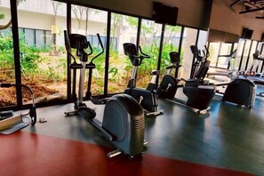 Una palestra con diverse macchine cardio, ampie finestre e vista sul verde circostante.