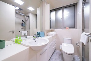 Un baño moderno con lavamanos blanco, espejo, ducha e inodoro.