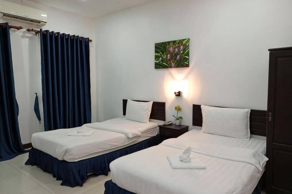 Habitación de hotel con dos camas individuales, una mesita de noche con lámpara, un cuadro en la pared y un armario.