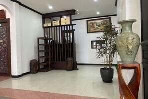 A reception area with a wooden gate, a potted plant, and a large vase on a stand. - Subinh Hotel (Pakse)