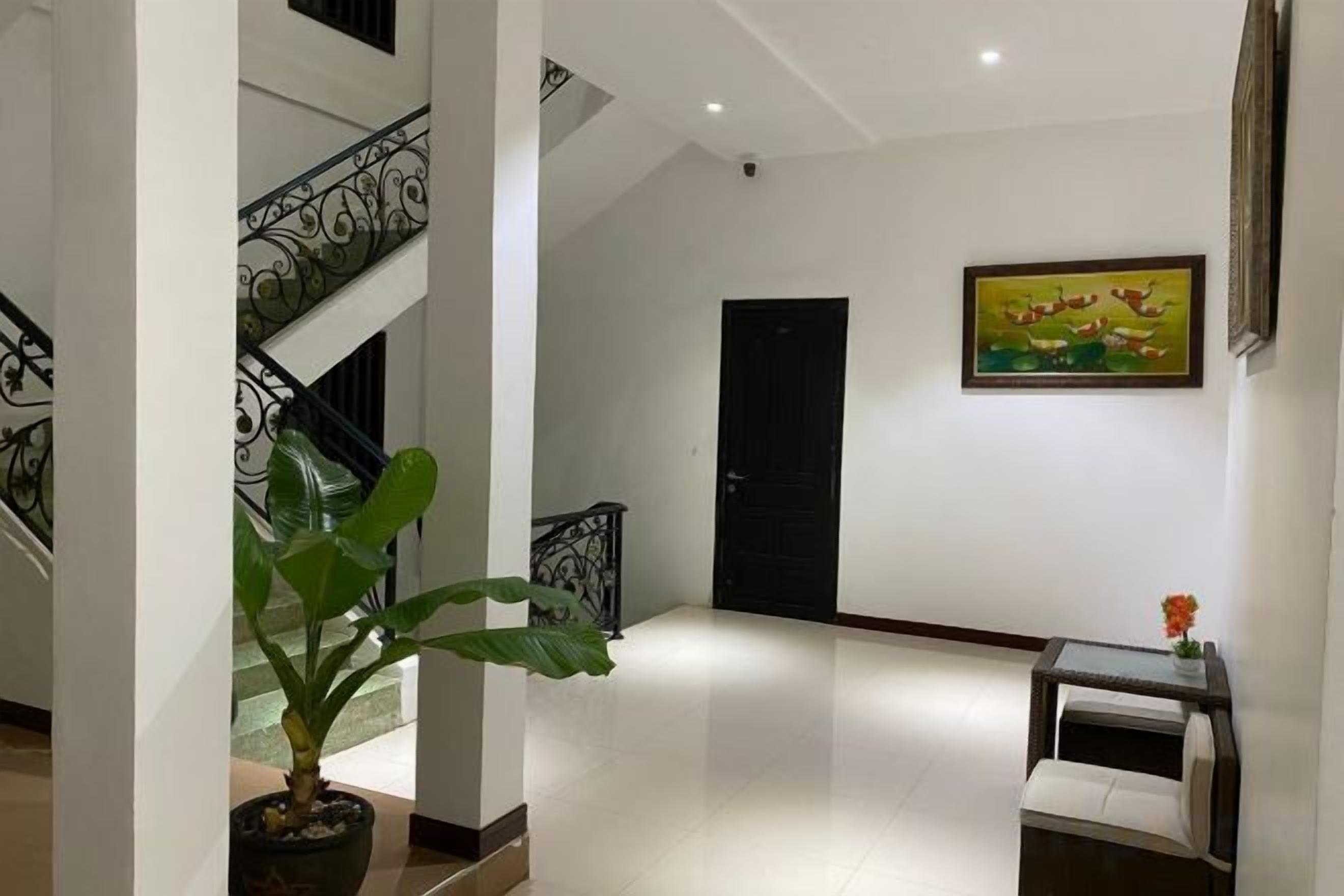 A hallway with a staircase, a door, a painting, and a desk with a vase.