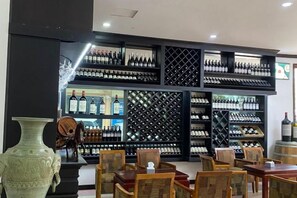 A wine cellar with shelves of wine bottles, wooden chairs, and a large vase.