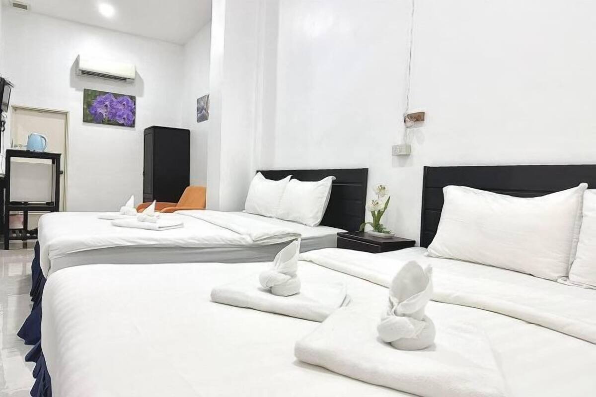 Habitación de hotel con dos camas, ropa de cama blanca, una mesita con lámpara y aire acondicionado instalado en la pared.