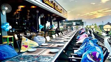 A restaurant with outdoor seating, a long table, and a view of the sky.