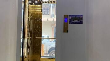 An elevator with a glass door, a digital display, and a sign with a nighttime scene.