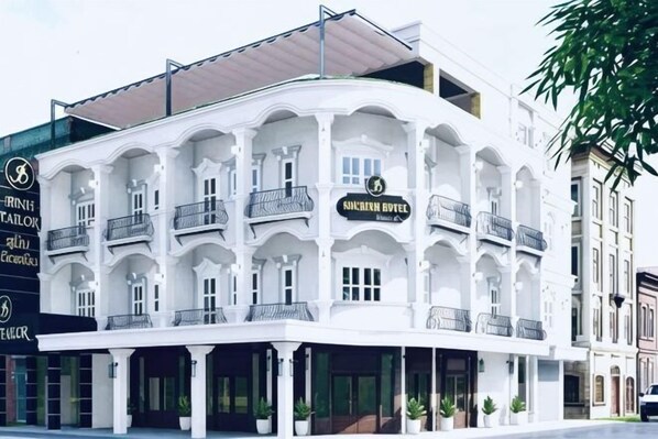 A white building with balconies, a sign reading 'ANCIEN BUREAU,' and a storefront with a sign that says 'BRINDI TAILOR.' - Subinh Hotel (Pakse)