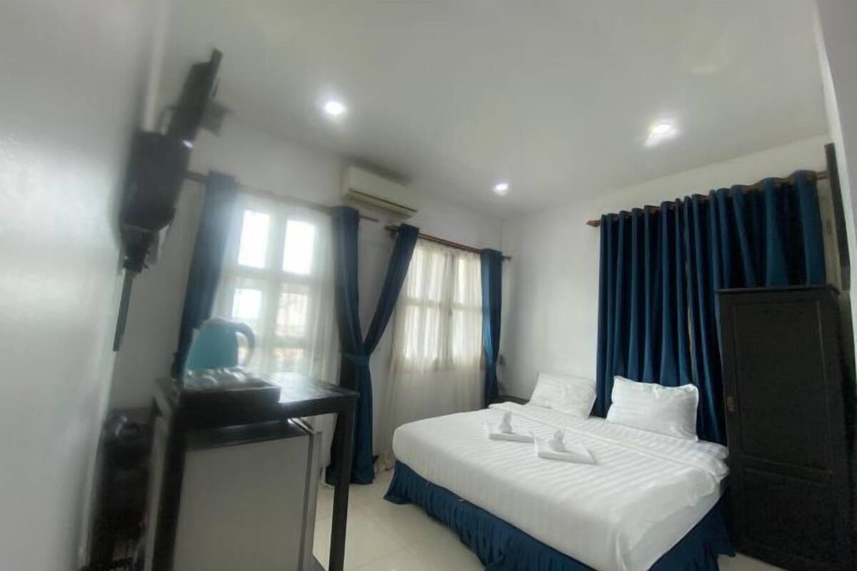 Un dormitorio con cama, escritorio, armario y ventana con cortinas.