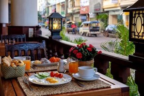 A breakfast table with eggs, tomatoes, bread, and juice, overlooking a street with cars and buildings.