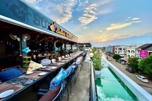 A restaurant with outdoor seating overlooking a street and a water feature. - Subinh Hotel (Pakse)