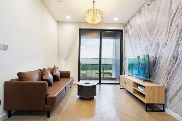 A modern living room with a brown sofa, a round coffee table, a wooden TV stand, and a large painting on the wall.