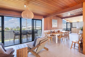 Una habitación amplia con techo de madera, ventanas grandes, un comedor con mobiliario de madera y vistas al exterior.