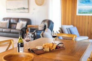 A wooden dining table with a bottle of wine, glasses, and a cheese board.