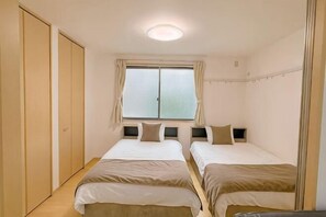 A bedroom with two beds, a window with curtains, and a wardrobe. - Urban Heights Watanabedori A (Fukuoka)