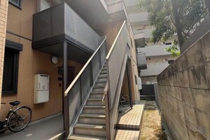 A residential building with a staircase leading to an upper floor, a bicycle parked outside, and a concrete wall.