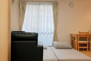 Una habitación con una cama, un sofá negro, una silla de madera, una mesita y un reloj en la pared.
