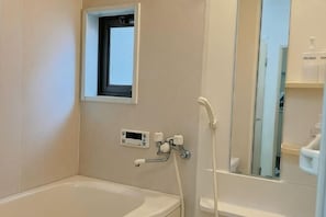 Une salle de bain avec une baignoire, une petite fenĂȘtre, un miroir et une douche.