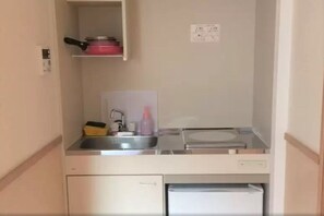 A compact kitchenette with a sink, a small refrigerator, and a shelf with a pot and a bottle. - Uenohouse Annex (Tokyo)