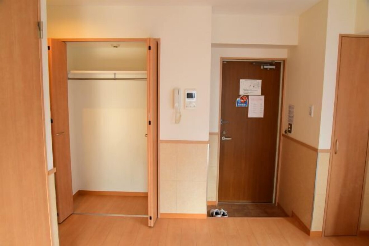 An empty room with a wooden floor, a closet, a door with a notice, and a wall-mounted phone.