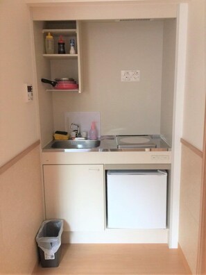 A compact kitchenette with a sink, a small refrigerator, and a trash bin. - Uenohouse Annex (Tokyo)